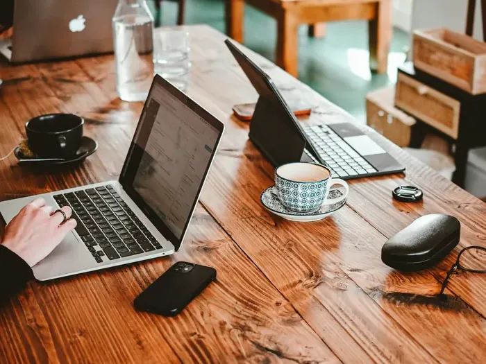 Open laptops, smartphone and coffee cups on a wooden table in a cozy coworking space used by small business teams